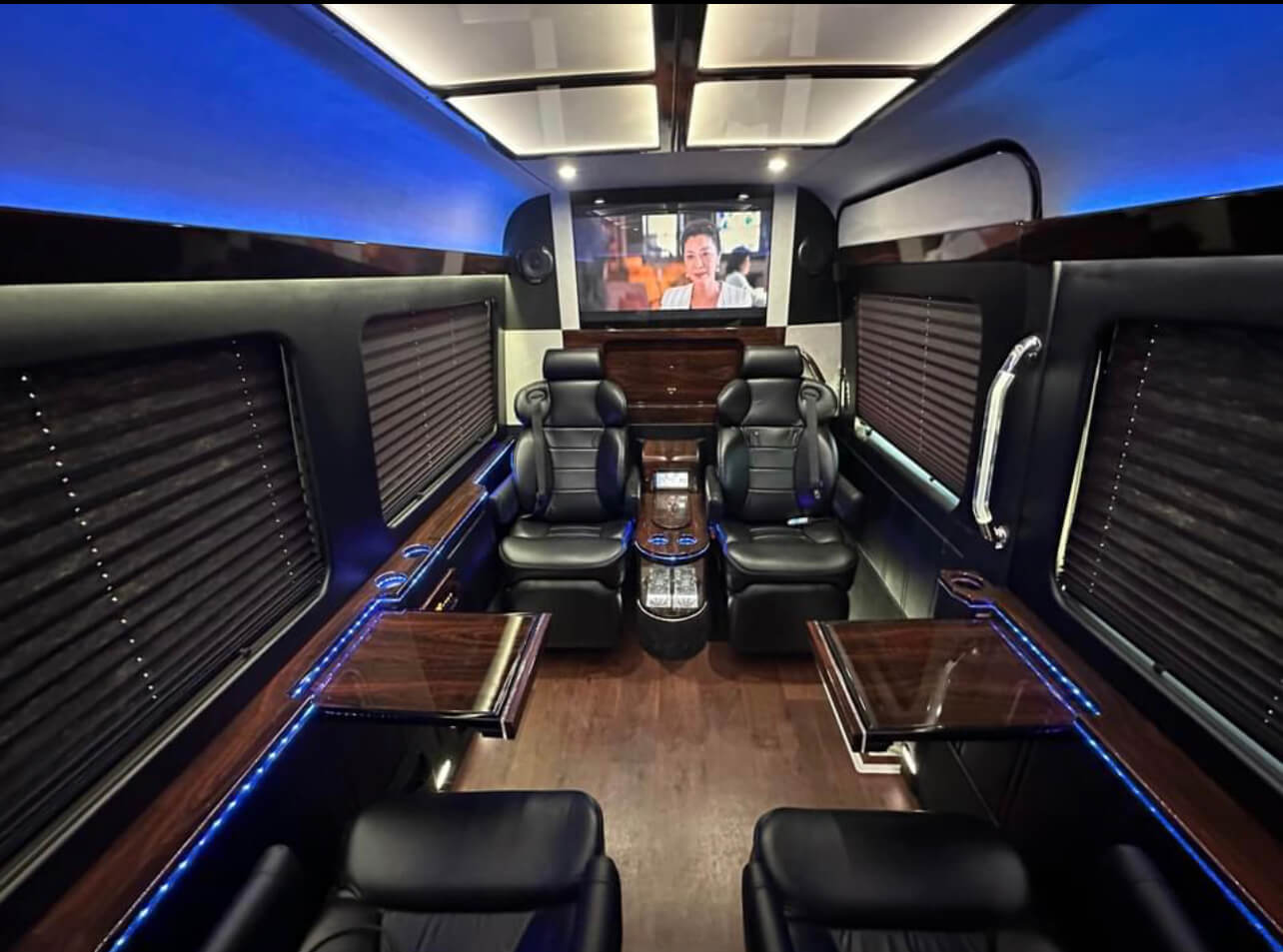 California Wine Tours luxury van interior with black leather seats, wood accents, TV screen, and ambient blue lighting