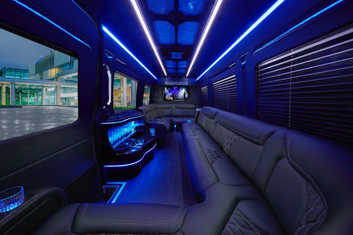 Luxury party bus interior with black leather seats, LED lights, glassware, and screen for corporate transportation in Napa.