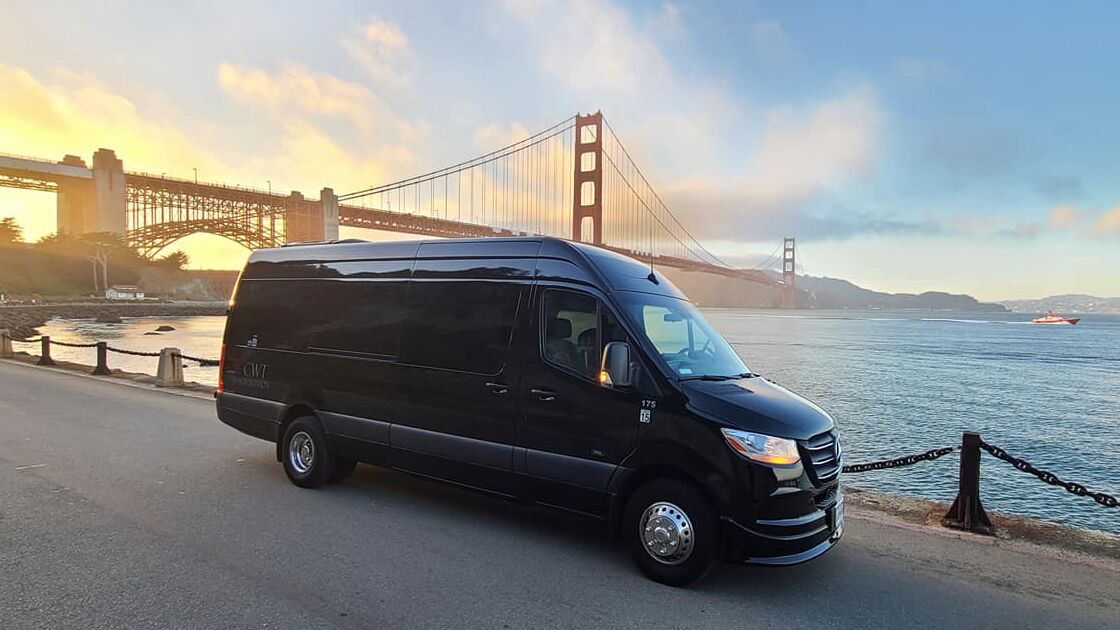 Black luxury sprinter van for corporate transportation in Napa, parked by Golden Gate Bridge at sunset with scenic backdrop.