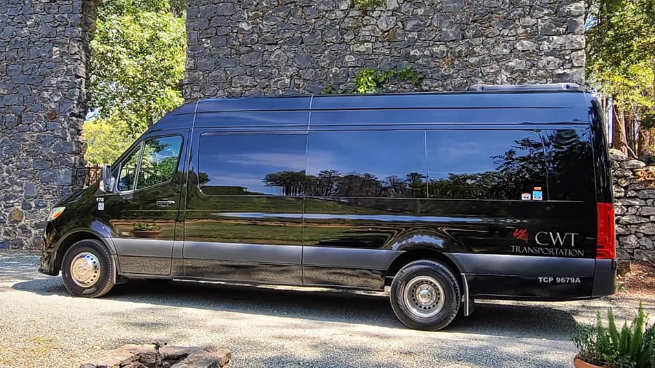 California Wine Tours black CWT luxury van parked beside historic stone wall in vineyard setting for wine tour travel