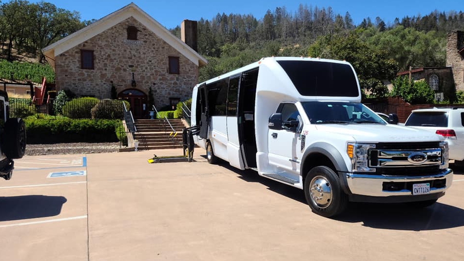 California Wine Tours white shuttle bus parked at historic winery entrance, providing group transportation for wine tours